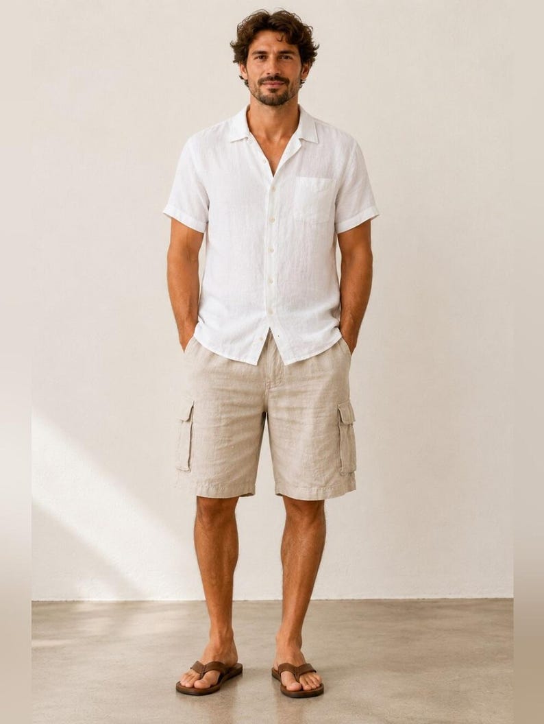 May include: A white short-sleeve shirt with a front pocket and beige cargo shorts. The shorts have two side pockets. The person is wearing brown sandals. The outfit is casual and suitable for warm weather.