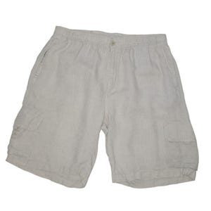 May include: Light beige cargo shorts made of a lightweight fabric. The shorts have an elastic waistband, a button closure, and two side pockets, along with two cargo pockets on the legs. The shorts are a neutral color.