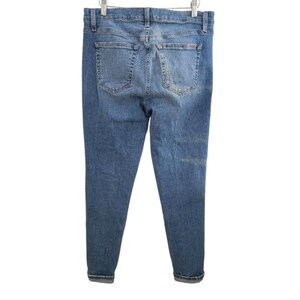 May include: Light blue denim jeans with a classic five-pocket design. The jeans are displayed from the back, showing the pockets, belt loops, and a faded wash effect. The cuffs are rolled up.