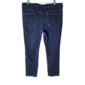 May include: Dark wash denim jeans with a classic five-pocket design, suspended from a wooden hanger. The jeans have a straight leg cut and gold-coloured hardware on the back pockets.