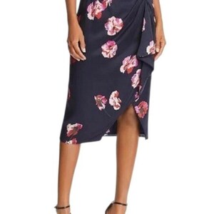 May include: Navy blue midi skirt with a floral pattern in shades of pink and white. The skirt features a wrap design with a side slit and is made of a smooth fabric. The skirt is knee-length.