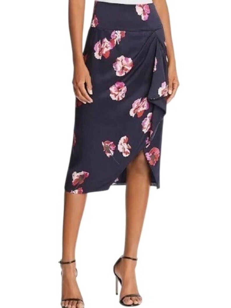 May include: Navy blue midi skirt with a floral pattern in shades of pink and white. The skirt features a wrap design with a side slit and is made of a smooth fabric. The skirt is knee-length.