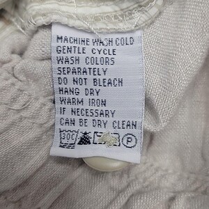 May include: White care label with black text instructions for washing, drying, and ironing a garment. The text reads "Machine Wash Cold, Gentle Cycle, Wash Colors Separately, Do Not Bleach, Hang Dry, Warm Iron, If Necessary Can Be Dry Cleaned".