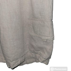 May include: A pair of light beige linen shorts with a large cargo pocket on the right side. The pocket has a flap with a button closure.