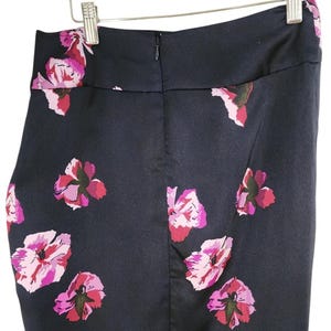 May include: A navy blue pencil skirt with a floral pattern of pink and magenta flowers. The skirt is hanging on a wooden hanger. The skirt has a zipper closure in the back.