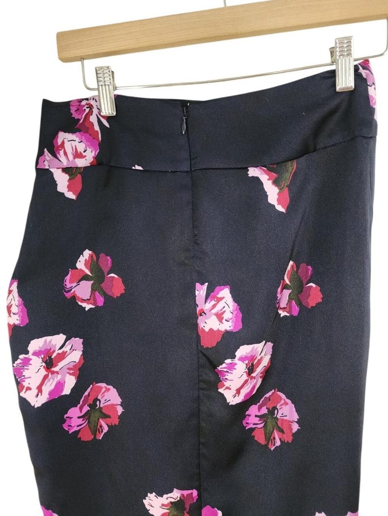 May include: A navy blue pencil skirt with a floral pattern of pink and magenta flowers. The skirt is hanging on a wooden hanger. The skirt has a zipper closure in the back.