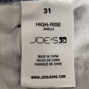 May include: A white clothing label featuring black text that reads 31, HIGH-RISE, JANELLE, JOE'S, MADE IN CHINA, HECHO EN CHINA, FABRIQU&Eacute; EN CHINE, and WWW.JOESJEANS.COM, sewn onto the inside of blue denim jeans with a clear woven fabric texture.