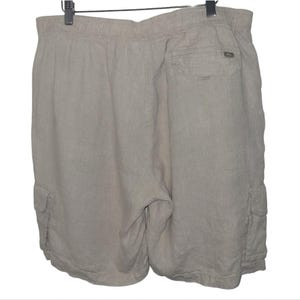 May include: Tan linen shorts with an elastic waistband and cargo pockets. The shorts are hanging on a black hanger. The shorts have a relaxed fit and are made of a lightweight fabric.