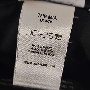 May include: A white tag with black text. The tag reads "THE MIA BLACK" and features the "JOE'S" logo. Below the logo, it states "MADE IN MEXICO, HECHO EN MEXICO, FABRIQUE AU MEXIQUE." The website www.joesjeans.com is also printed on the tag.