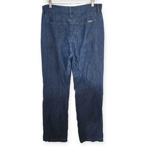May include: A pair of medium-wash blue denim jeans featuring a high-waisted design, a button and zip fly closure, two back patch pockets, and a small rectangular metal brand tag attached to the upper right back pocket area.