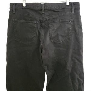 May include: Black denim jeans with two back pockets and a classic five-pocket design. The jeans are hanging on a white background. The jeans have a straight leg cut and a button and zipper closure.