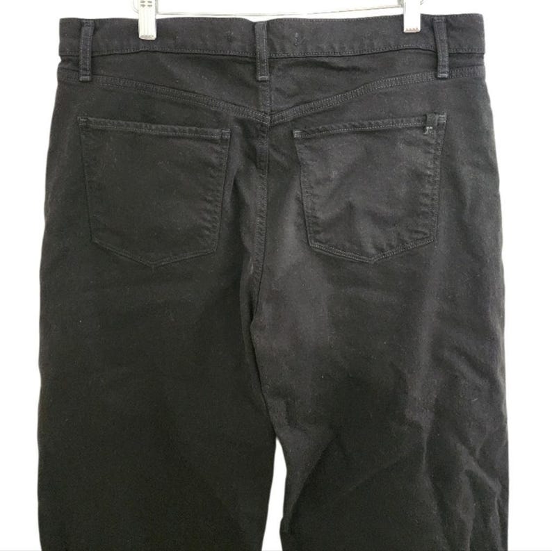 May include: Black denim jeans with two back pockets and a classic five-pocket design. The jeans are hanging on a white background. The jeans have a straight leg cut and a button and zipper closure.