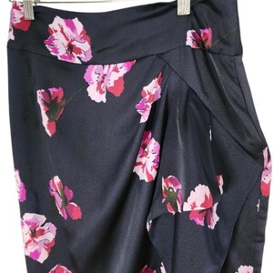 May include: A navy blue skirt with a floral pattern of pink and red flowers. The skirt is made of a shiny, silky material and is hanging on a wooden hanger.