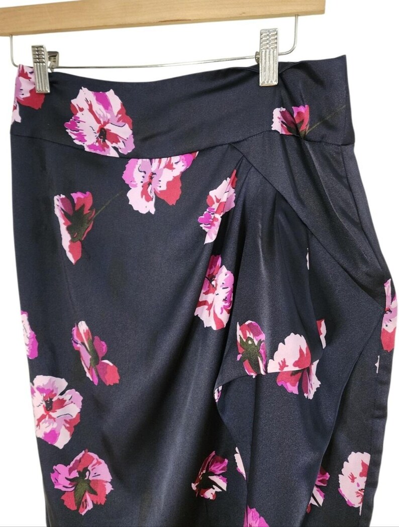 May include: A navy blue skirt with a floral pattern of pink and red flowers. The skirt is made of a shiny, silky material and is hanging on a wooden hanger.
