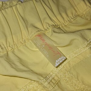 May include: Close-up of yellow shorts. The shorts have a drawstring waist and a tag that reads "for movement" and "made in china". The fabric appears to be lightweight.