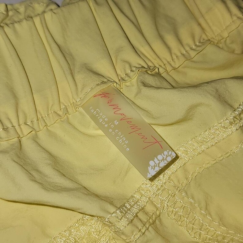 May include: Close-up of yellow shorts. The shorts have a drawstring waist and a tag that reads "for movement" and "made in china". The fabric appears to be lightweight.