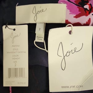 May include: Close-up of a navy blue garment with floral print, featuring multiple tags. The tags display the brand name "Joie", style information, and size 2. The garment's color is listed as "Midnight".
