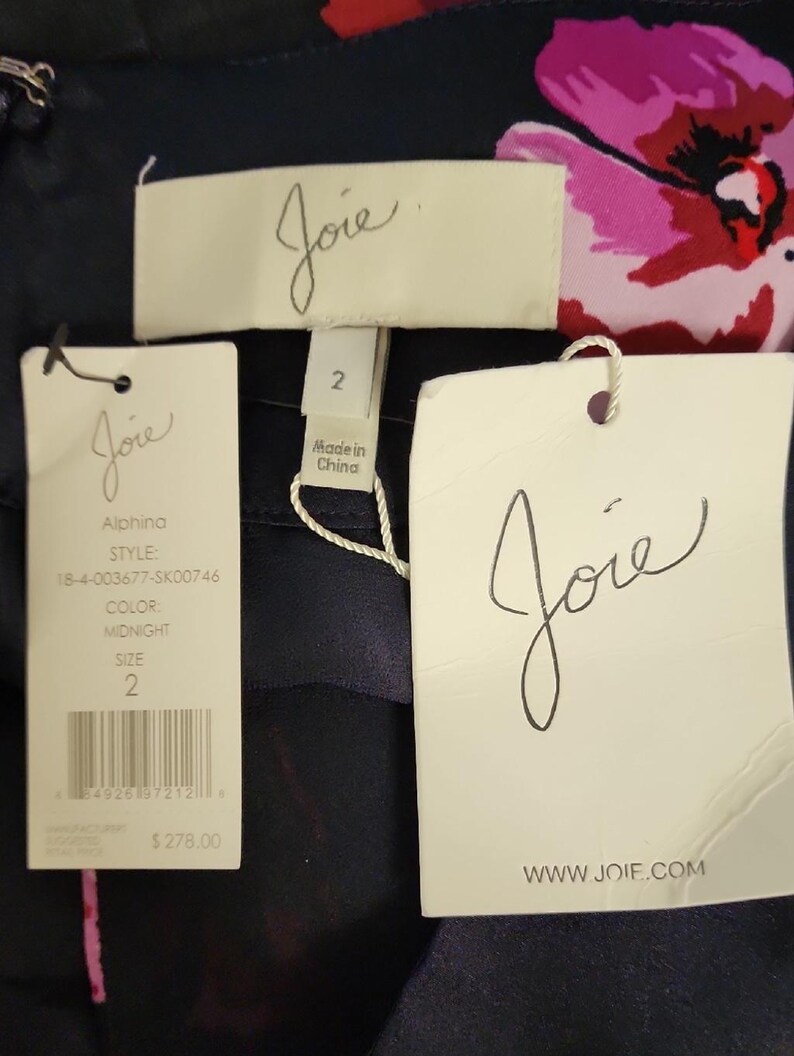 May include: Close-up of a navy blue garment with floral print, featuring multiple tags. The tags display the brand name "Joie", style information, and size 2. The garment's color is listed as "Midnight".