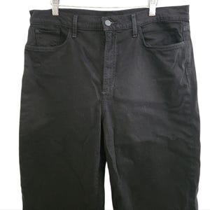 May include: Black denim pants with a classic five-pocket design. The pants have a button and zipper closure and are hanging on a white hanger. The fabric appears to be a medium weight denim.