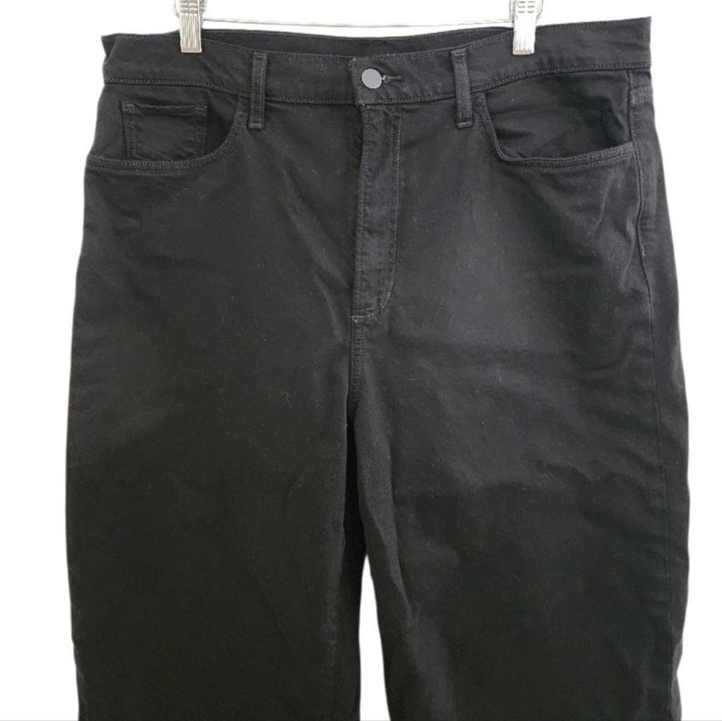 May include: Black denim pants with a classic five-pocket design. The pants have a button and zipper closure and are hanging on a white hanger. The fabric appears to be a medium weight denim.