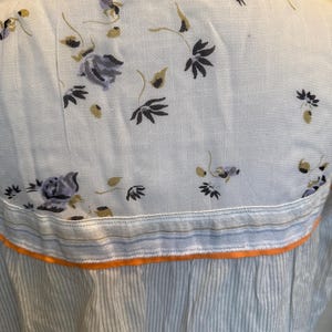 May include: A white button-down shirt with a floral print and a blue and white striped bottom. The shirt has an orange trim.