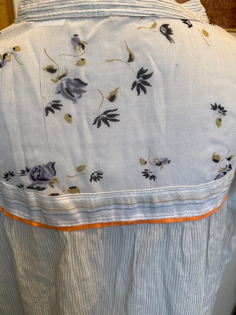 May include: A white button-down shirt with a floral print and a blue and white striped bottom. The shirt has an orange trim.