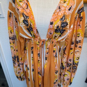 May include: A long, orange maxi dress with a floral print and white stripes. The dress has a deep V-neckline and long sleeves.