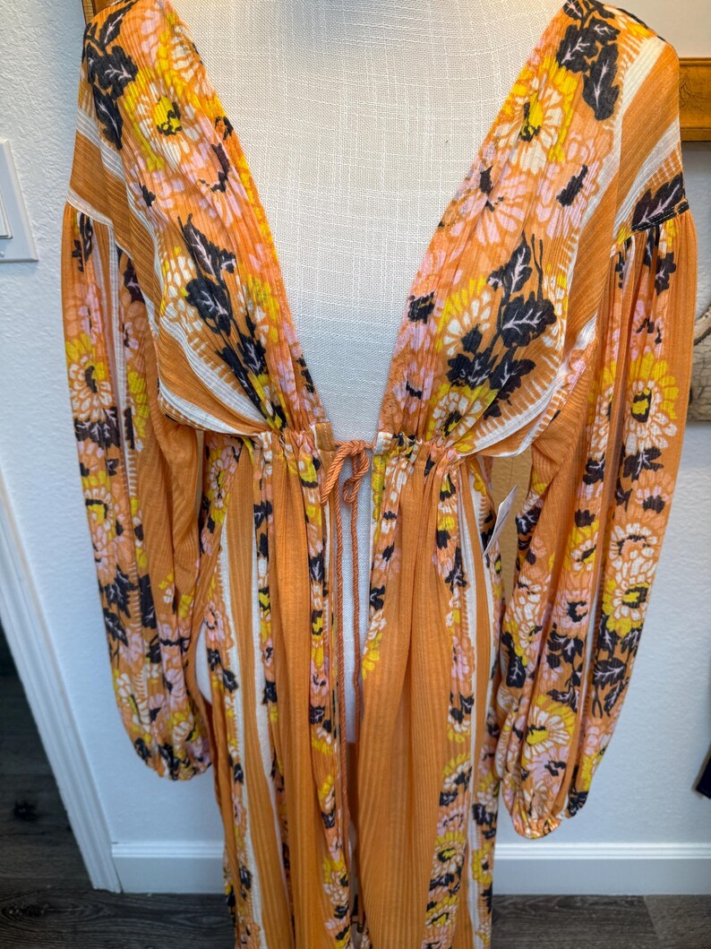 May include: A long, orange maxi dress with a floral print and white stripes. The dress has a deep V-neckline and long sleeves.