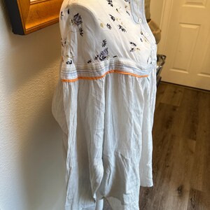May include: A white and blue striped long-sleeved shirt with a floral print on the top half. The shirt has a button-up collar and a button closure.