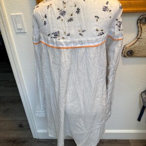 May include: A white and gray striped long-sleeved shirt with a floral pattern on the back. The shirt has a mandarin collar and a button-up front.