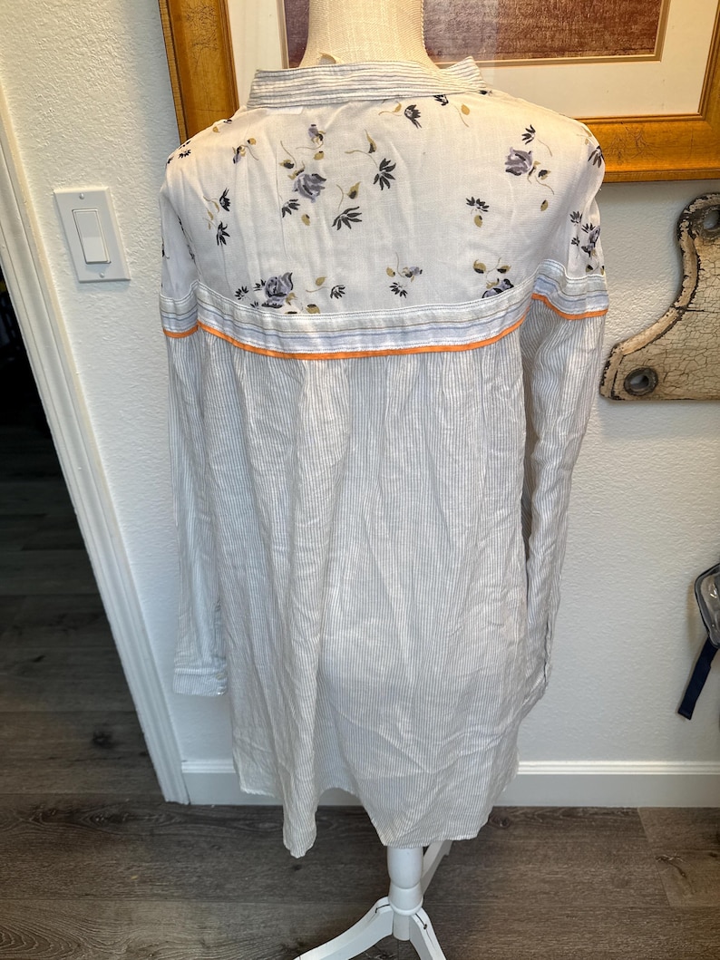 May include: A white and gray striped long-sleeved shirt with a floral pattern on the back. The shirt has a mandarin collar and a button-up front.