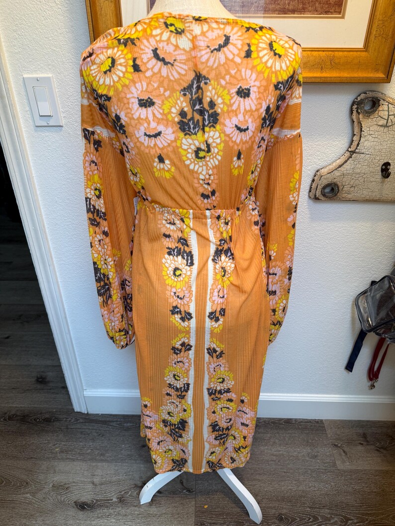 May include: A long, orange maxi dress with a floral print. The dress has a V-neckline, long sleeves, and a fitted waist. The floral print features pink, yellow, and black flowers on a light orange background.
