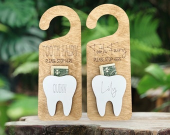 May include: Two wooden door hangers with a slot for money, designed for the Tooth Fairy. Each has a tooth-shaped cutout and the words "Tooth Fairy PLEASE STOP HERE". One says "Quinn" and the other says "Lily".