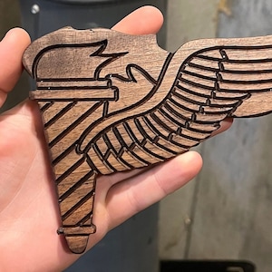Puede incluir: Un ala de madera tallada con un diseño estilizado de un rayo y un ala. El ala está hecha de madera oscura y tiene un diseño detallado.
