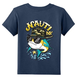 May include: A navy blue short-sleeve t-shirt featuring a graphic of a fish wearing a camouflage baseball cap and black sunglasses. The text "NAUTI BOY" is printed in yellow above the fish, with "Wild Little Ones" written below it.