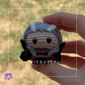 Puede incluir: Muñeca de ganchillo hecha a mano con un atuendo gris y negro, ojos negros y mejillas rosadas. La muñeca tiene una cara marrón claro y cabello gris con detalles blancos. El texto "CHICKURIMI" es visible.