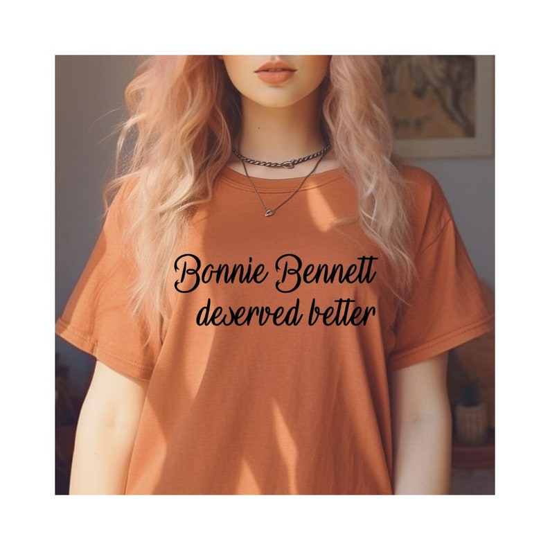May include: A brown t-shirt with the text "Bonnie Bennett deserved better" printed in black cursive font.