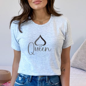 May include: A heather grey t-shirt with a black spade and the word "Queen" in a script font.