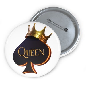 May include: A white button with a black spade design and a gold crown on top. The spade has the word "QUEEN" written in gold letters.