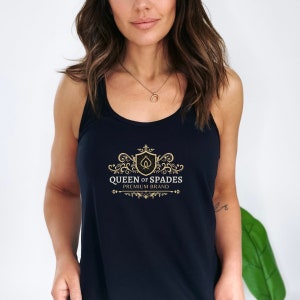 May include: A black tank top with a gold logo that says "Queen of Spades Premium Brand". The logo features a stylized spade card with a crown on top.