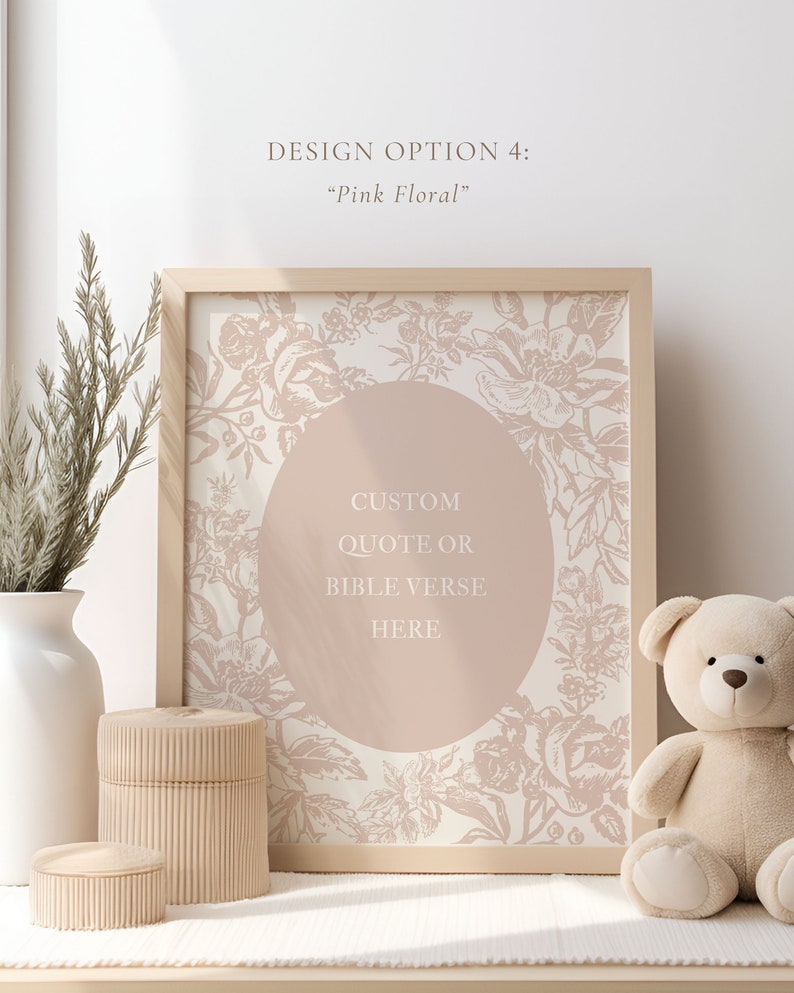 以下が含まれることがあります： ピンクの花柄のデザインと中央に「CUSTOM QUOTE OR BIBLE VERSE HERE」というテキストが書かれた円形が描かれた額装されたプリント。プリントは、白い花瓶、木製の箱、テディベアのあるテーブルの上に置かれています。