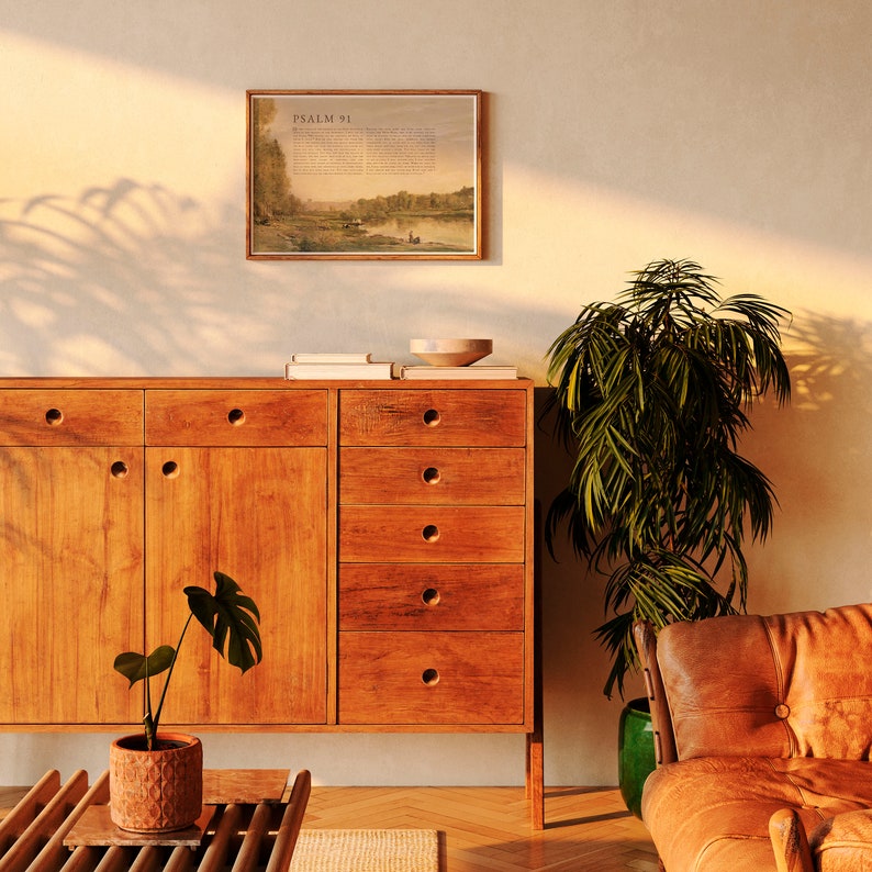 May include: A wooden cabinet with six drawers and two doors. The cabinet is a light brown color and has a modern design. A potted plant sits on the floor in front of the cabinet. A framed print with the text "PSALM 91" hangs on the wall above the cabinet.