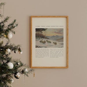 May include: A framed print with the text "COME, THOU LONG EXPECTED JESUS". The image shows sheep in a snowy landscape with trees and mountains. The print has a light wood frame and is hanging on a neutral wall.