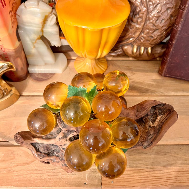 May include: A cluster of amber glass grapes on a piece of driftwood. The grapes are arranged in a realistic way, with some grapes hanging down and others clustered together.