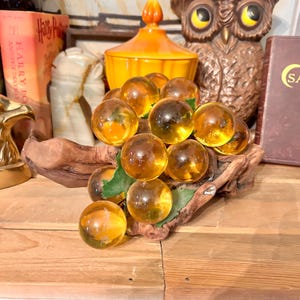 May include: A cluster of amber glass grapes on a piece of driftwood. The grapes are arranged in a bunch and have a realistic appearance.