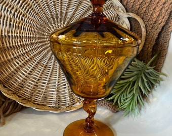 May include: A vintage amber glass candy dish with a lid and a twisted stem. The dish has a decorative, faceted design.