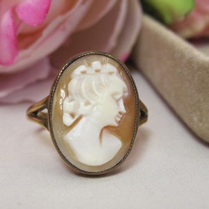 May include: A gold ring with a cameo of a woman's profile in white shell. The cameo is set in an oval frame.