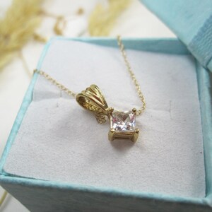 May include: A gold chain necklace with a square-shaped pendant featuring a clear cubic zirconia stone.