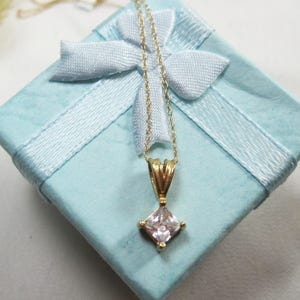 May include: A gold necklace with a square-shaped pendant featuring a clear cubic zirconia stone. The necklace is displayed in a light blue gift box with a white satin ribbon.
