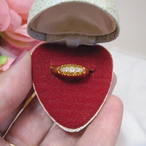 May include: A gold ring with a row of small diamonds set in the band. The ring is in a red velvet heart-shaped box.